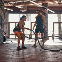 Tuinposter Man look at girl exercise with sports rope in gym © Svitlana