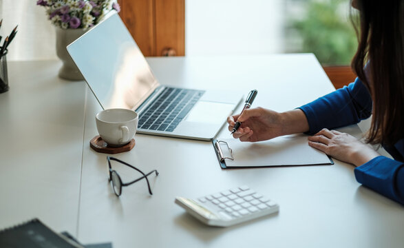 Cropped photo of woman writing making list taking notes in notepad working or learning on laptop indoors- educational course or training, seminar, education online concept