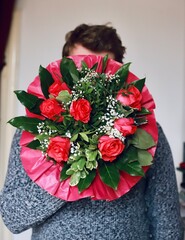 A man holding a bouquet of red roses in front of his face