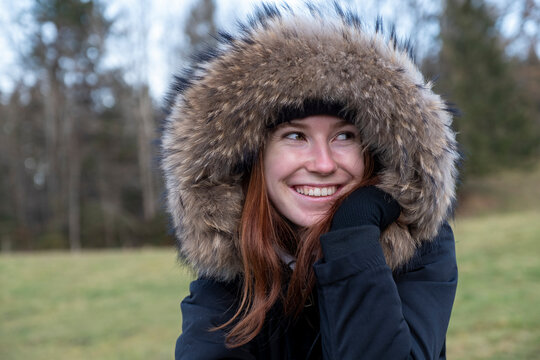 Smiling young woman with warm fur hooded coat looking away in nature