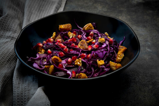 Studio shot of bowl of vegan salad with red cabbage, pomegranate seeds, dried figs and walnuts