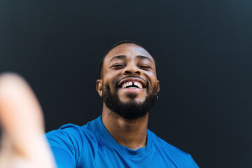 Cheerful athlete with gap teeth taking selfie against black background