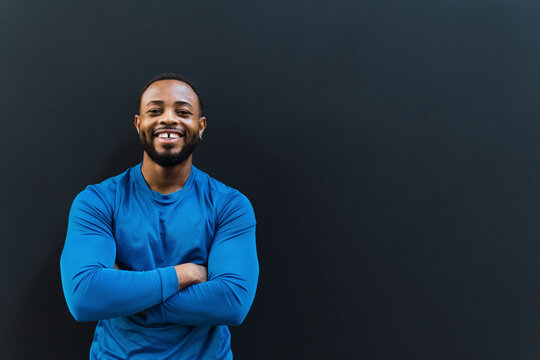 Happy sportsman with arms crossed against black background