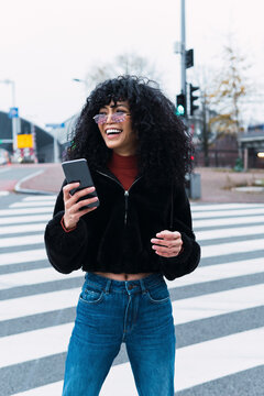Happy young woman holding smart phone standing on road marking