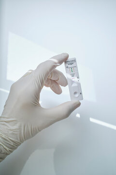 Hand Holding Rapid Diagnostic Device With COVID-19 Positive Results Against White Background