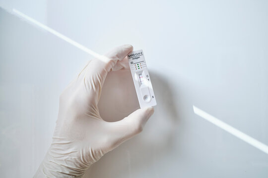 Hand holding rapid diagnostic device showing COVID-19 positive results against white background