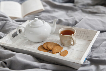 Fototapeta na wymiar interior and home coziness concept. Top view. A cup of tea, a teapot with herbal tea, sugar bowl on a wooden tray on the bed. Porcelain cup