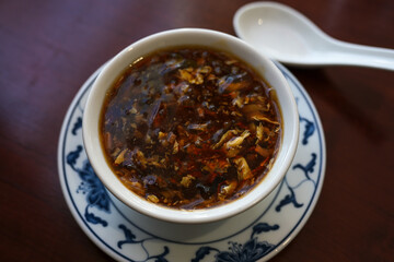 Chinese soup spicy and sour in a bowl with porcelain spoon on a brown table, selected focus