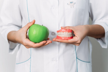 A false denture and a green apple in the hands of a dentist. Dental prosthesis care. A denture and an apple in the hands of an orthopedic dentist. Dental care. Prosthetics. False teeth