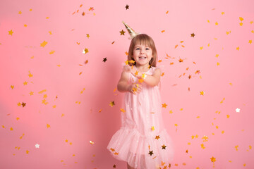 Obraz na płótnie Canvas happy child girl in dress having fun with confetti and celebrating her birthday on pink background