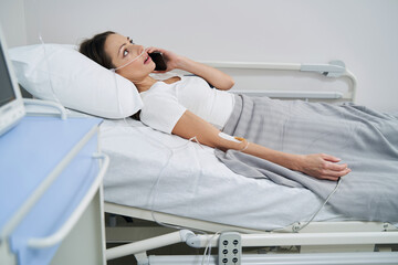 Patient lying in bed in hospital ward during phone conversation