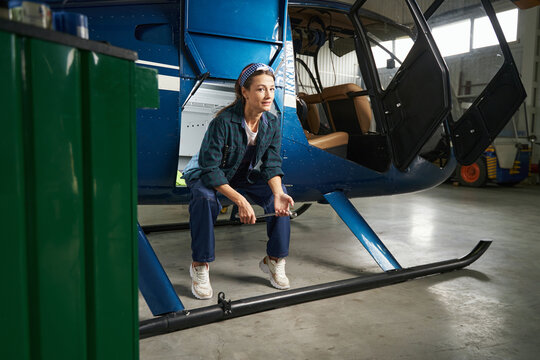 Joyful female mechanic in uniform resting during the break in aviation hangar
