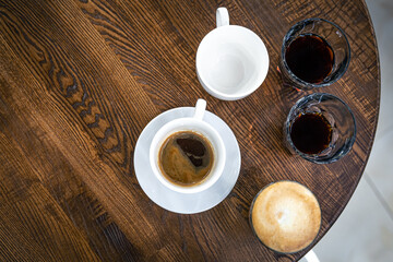 Coffee in a cup and in glasses on a wooden table, top view.