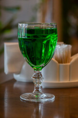 transparent glass with a wine drink on a wooden table. Bright green drink in a glass