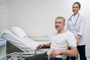Fototapeta premium Cheerful kinesiologist and patient posing for camera in hospital ward