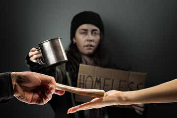 Man gives a stack of cash to woman, hands close up. Defocused begging woman holds a cardboard sign with the text homeless on the background. The concept of helping the hobos and vagrants