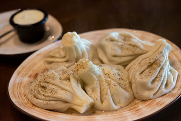 khinkali - traditional Georgian dumplings in a white plate with white sour cream sauce on a wooden table in the restaurant