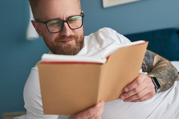 Positive man reading book at home - obrazy, fototapety, plakaty