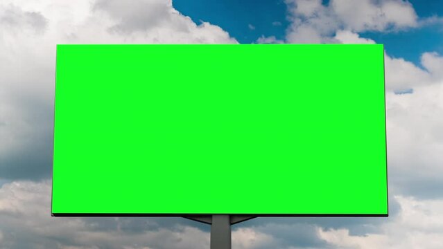 Front view: blank green billboard or large advertising display and moving white clouds against blue sky - timelapse. Chroma key, green screen, template, mock up, copy space and time lapse concept