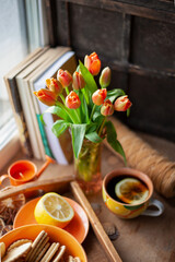 Still life on the table. Bouquet of red tulips and tea with lemon in a cup. Vase.