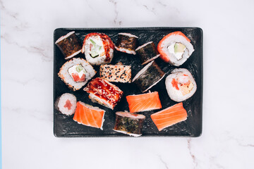 Sushi bar lunch menu - top view on different sushi rolls with salmon, avocado and smocked eel on white marble table background. Online order delivery food online, takeout food concept