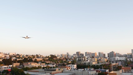Airplane landing to San Diego airport, California USA. Under plane arriving at sunset, city skyline or downtown urban cityscape. Skyscrapers and aeroplane or aircraft. Airliner flying mid air in sky. - obrazy, fototapety, plakaty