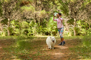 girl playing ball with a cute fluffy japanese spitz puppy dog on natural background in a forest or park