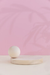 Minimal abstract background with a premium podium for the presentation of a cosmetic product. Wooden scenes of different geometric shapes on a beige table on a pink background with a shadow of leaves.