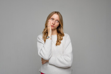 Fototapeta na wymiar Young blonde woman wearing cozy white sweater, thinking looking tired and bored with depression problems, standing against gray background