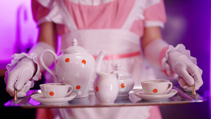 Pink maid with gloves carry tray with retro tea cups close-up