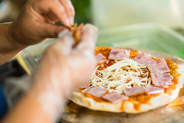 The chef is preparing the pizza with ham before putting it in the oven. use traditional firewood