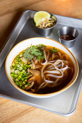 Japanese ramen soup with chicken, mushrooms, onion and sprout served in a plate on a metal tray.
