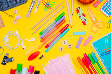 Series of stationery items for kids, colored pens, labels, paper clips, masks on yellow background, back to school concept, flat lay