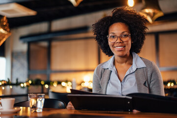 Portrait of an African-American woman with glasses, trying out the new food in a restaurant.