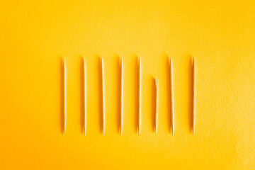 Series of toothpicks arranged in a row with one of them broken, concept of diversity and inclusion, yellow background - obrazy, fototapety, plakaty