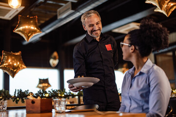 Friendly caucasian waiter, brinking a meal to his african-american female customer.