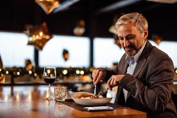 Lovely adult caucasian bearded man, noticing his ringing phone, next to his plate.
