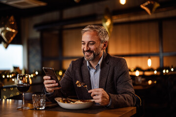Joyful adult man, receiving a lovely message, during his meal, on his phone.