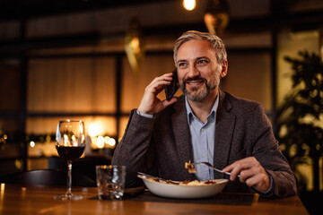 Relaxed adult caucasian man, having a conversation over his phone, during a meal.