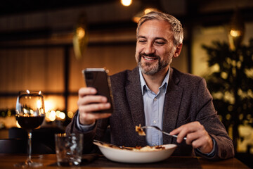 Lovely adult caucasian man in a suit, taking photos of his meal.