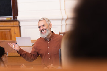 Smiling teacher holding chalkboard near blurred students in auditorium of university