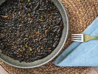 Black rice, paella served at a table - obrazy, fototapety, plakaty