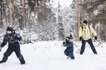 Father and sons having fun snowball fight together in winter forest. Happy children playing in snow...