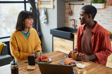 Portrait of smiling mixed-race couple enjoying breakfast at table in cozy home kitchen