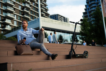 Businessman using the phone while sitting on the stairs. Happy man using the phone