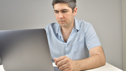 A man is typing on a laptop standing on a table