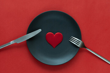 Black plate, knife and a fork with red heart. Romantic date concept, top view
