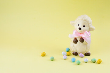 White Easter sheep figure made of white chocolate with small chocolate eggs on yellow background. Easter stock image with copy space