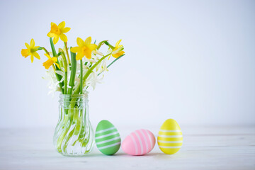 Yellow daffodils, white hyacinth flowers in crystal vase and three Easter eggs on wooden tabletop. Image with copy space