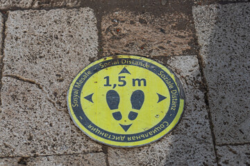 yellow sign with a call to keep social distance in Russian, English and German on the city pavement